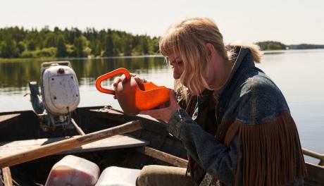 Nainen istuu soutuveneessä ja juo äyskäristä sahtia
