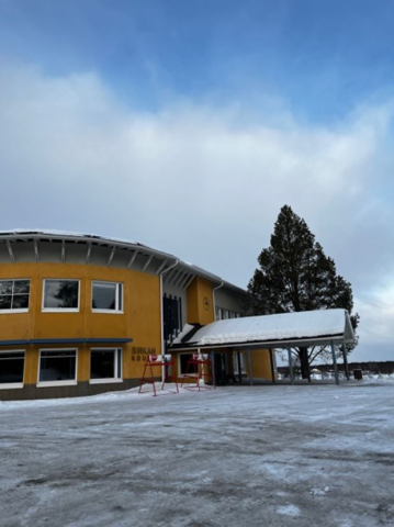 Sirkan koulun julkisivu on keltainen. Pääsisäänkäynnin katoksen päällä on lunta. Piha on tasainen. Taustalla näkyy iso kuusi.