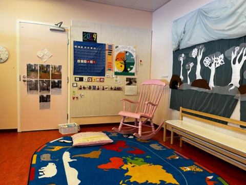 Huoneessa on nojatuoli, matto ja lasten piirrustuksia seinällä.