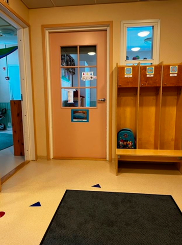 Huoneessa on kuramatto ja kuvan vasemmassa nurkassa on kaksi ovea toisiin huoneisiin. Edessä näkyy lasten naulakoita.