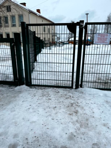 Metallinen portti lumisella taustalla. Portin takana on suuri talo.