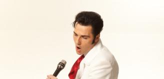 Laulaja Aron pukeutuneena Elvikseksi laulaa mikrofoniin valkoisessa puvussa