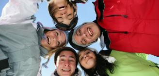 Nuoria ihmisiä hiihtovaatteissa, päät yhdessä, hymyilevät, kasvoja kuvassa kuvattuna alhaaltapäin