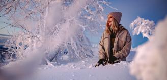 Hymyilevä pitkähiuksinen ihminen istuu lumessa lumisessa maisemassa