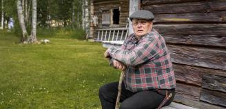 Syytinkiläinen istuskelemassa penkillä keppiin nojaillen