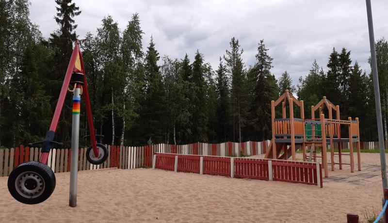 Aholanperän leikkipuisto, keinu ja kiipeilyteline, aitaa hiekkakentällä