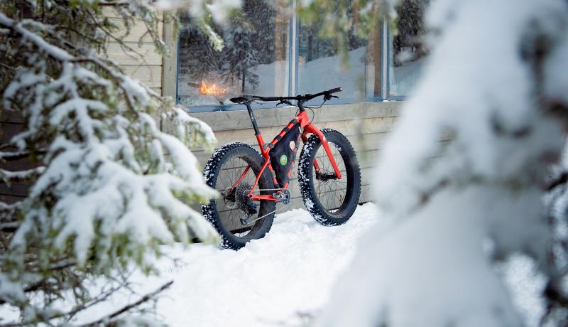 Fatbike nojaa tuvan seinään reitillä talivsessa maisemassa.